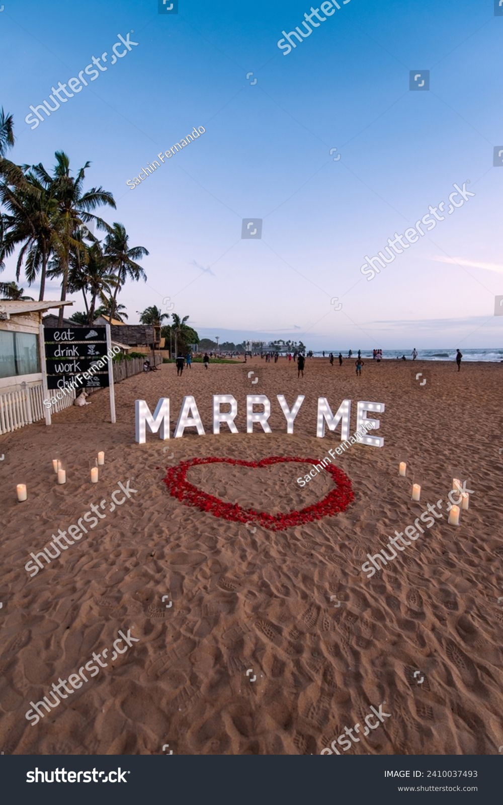 Marry me decoration lights with heart shaped flower petals on sand in a beautiful evening #2410037493