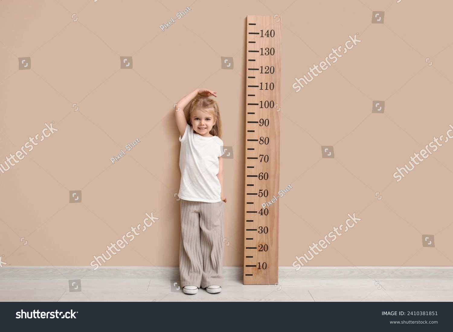 Cute little girl measuring height near beige wall #2410381851