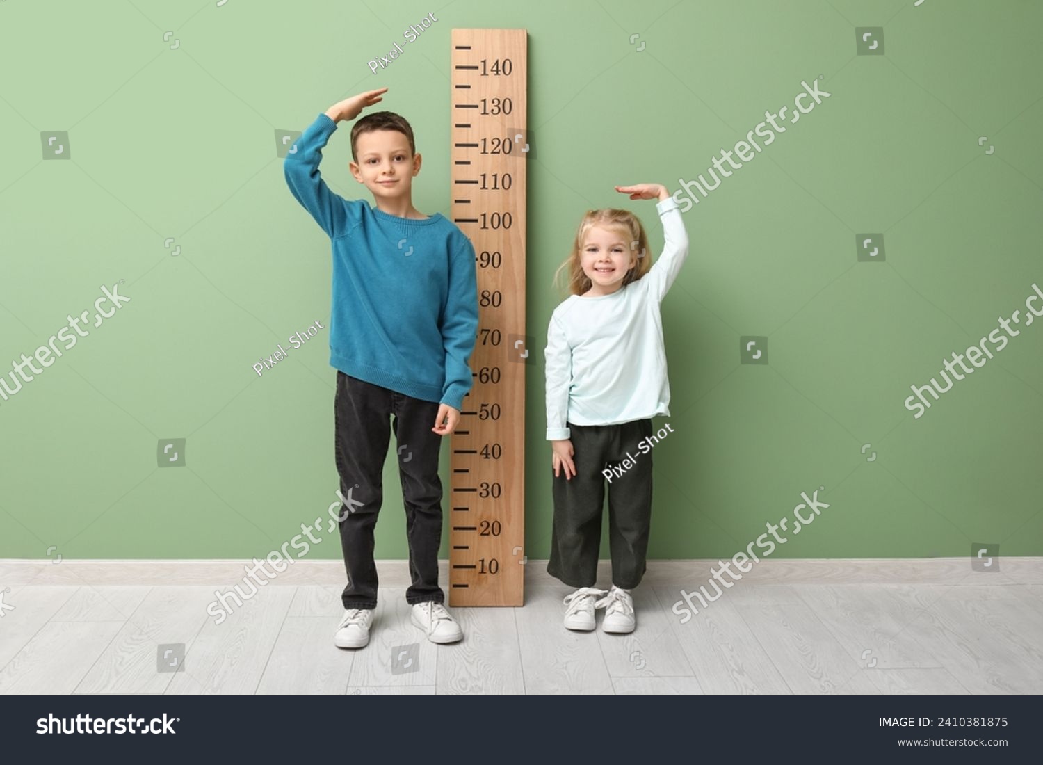 Cute little children measuring height near green wall #2410381875