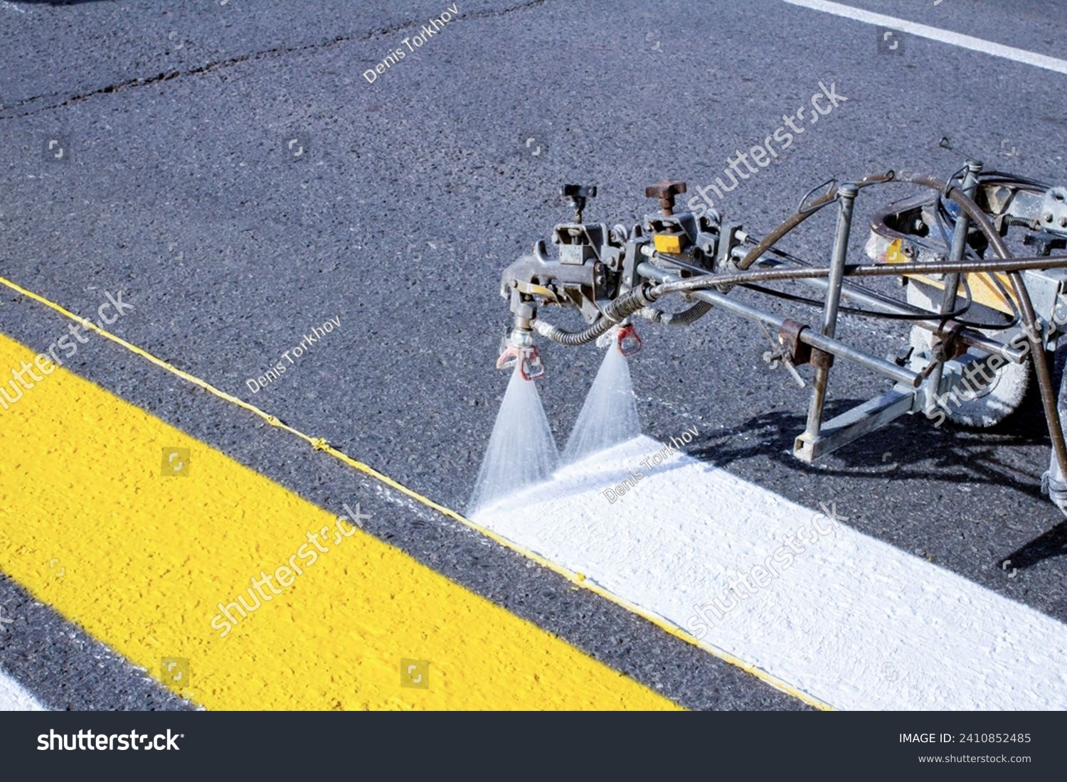 a team of workers drawing a pedestrian crossing in early spring using automated equipment on fresh asphalt #2410852485