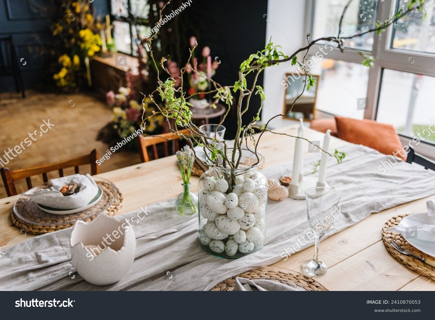 Easter decor closeup. Setting table for Easter dinner with candles, ceramic plates with easter eggs in nest, Easter bunny made of linen napkin. Holidays celebration concept. Side view. Set up. #2410870053