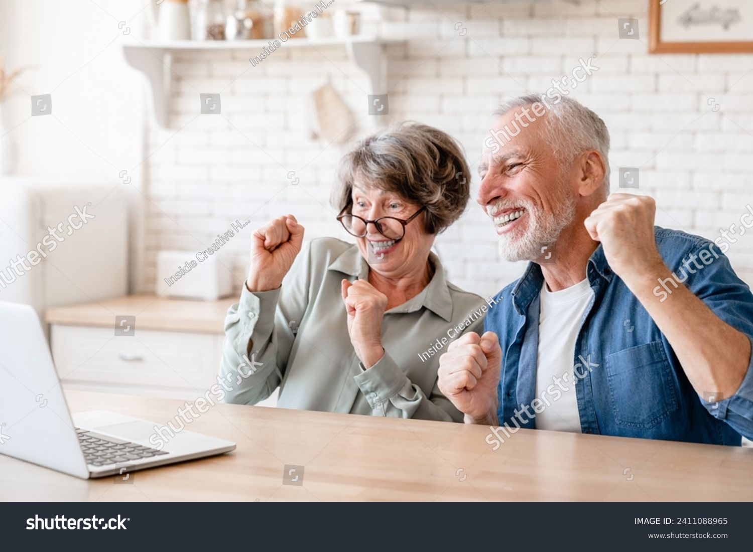 Caucasian senior old elderly couple husband and wife spouses grandparents watching movie, celebrating, winning, victory, cheering the prize from bidding online casino bets with laptop #2411088965