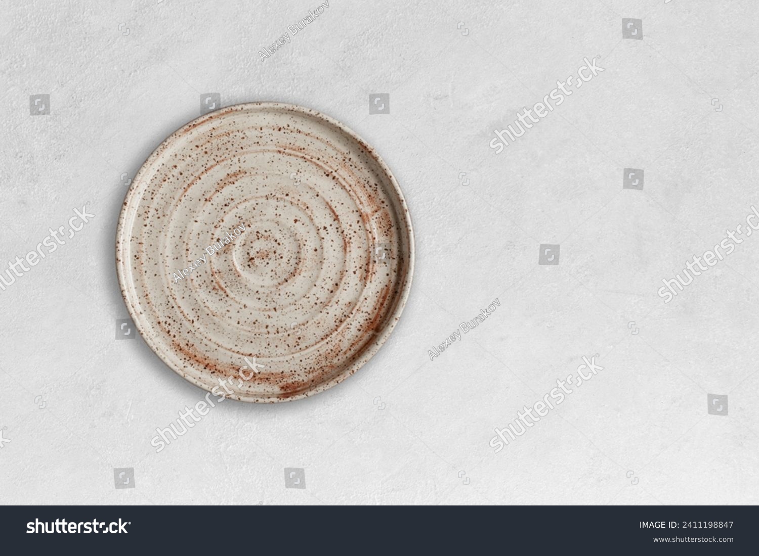 Handmade empty ceramic plate top view with copy space on grey concrete table. Minimalism. Eco friendly ceramics handcraft tableware. #2411198847