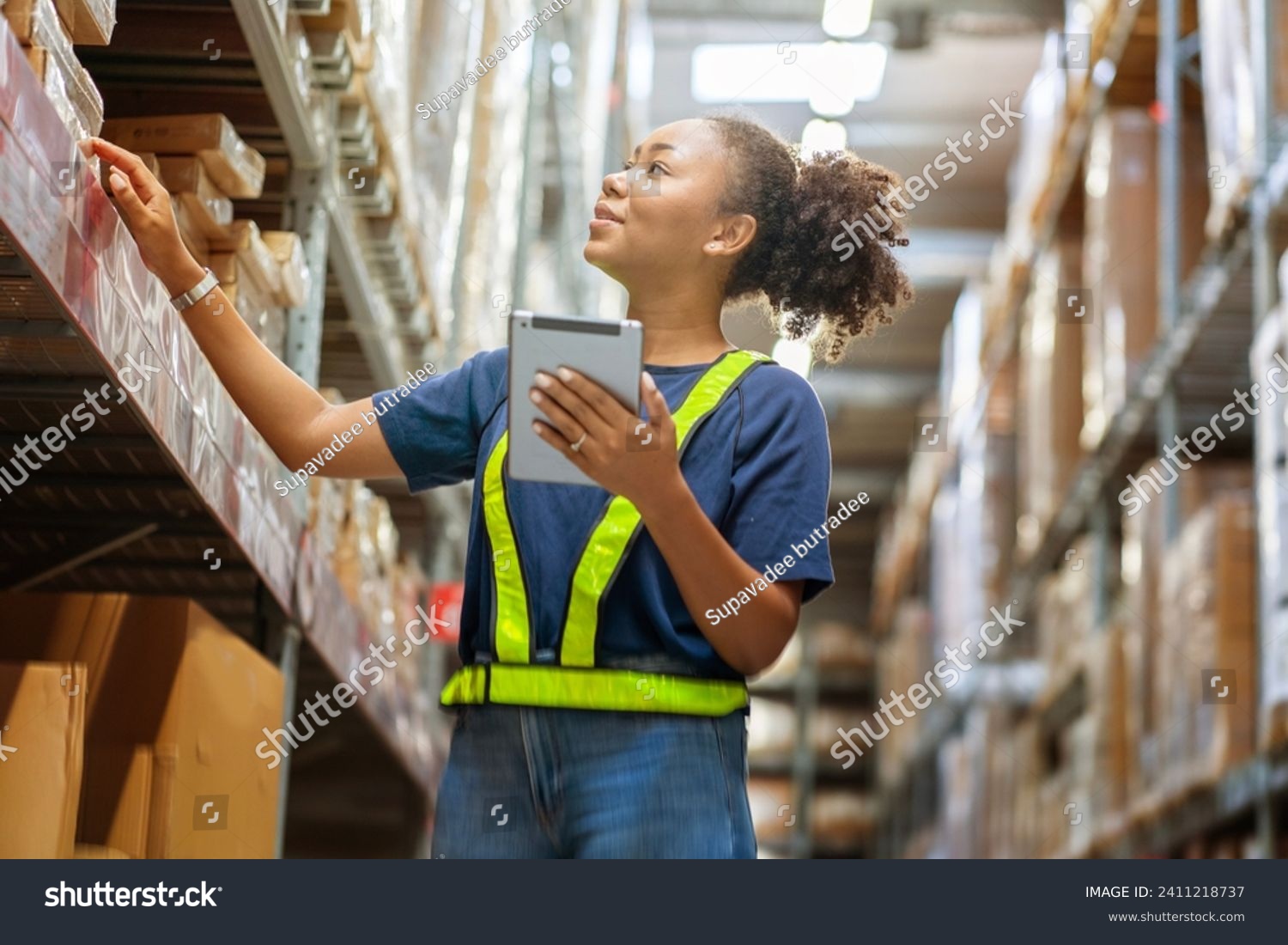 Young black African American woman holding a tablet checks inventory and checks orders from customers to deliver documents to customers in a warehouse wholesale store. #2411218737