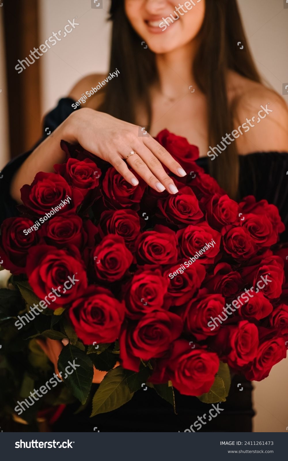Engagement ring. Marriage proposal. Elegant floral template for design for Valentine's Day. A girl's hand with a wedding ring on a big bouquet of red roses. Love concept. Closeup. Side view. #2411261473