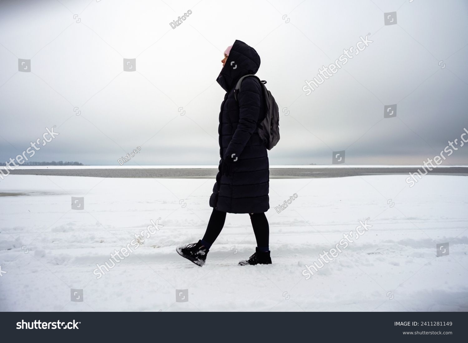 A woman walks along a snowy winter river bank #2411281149