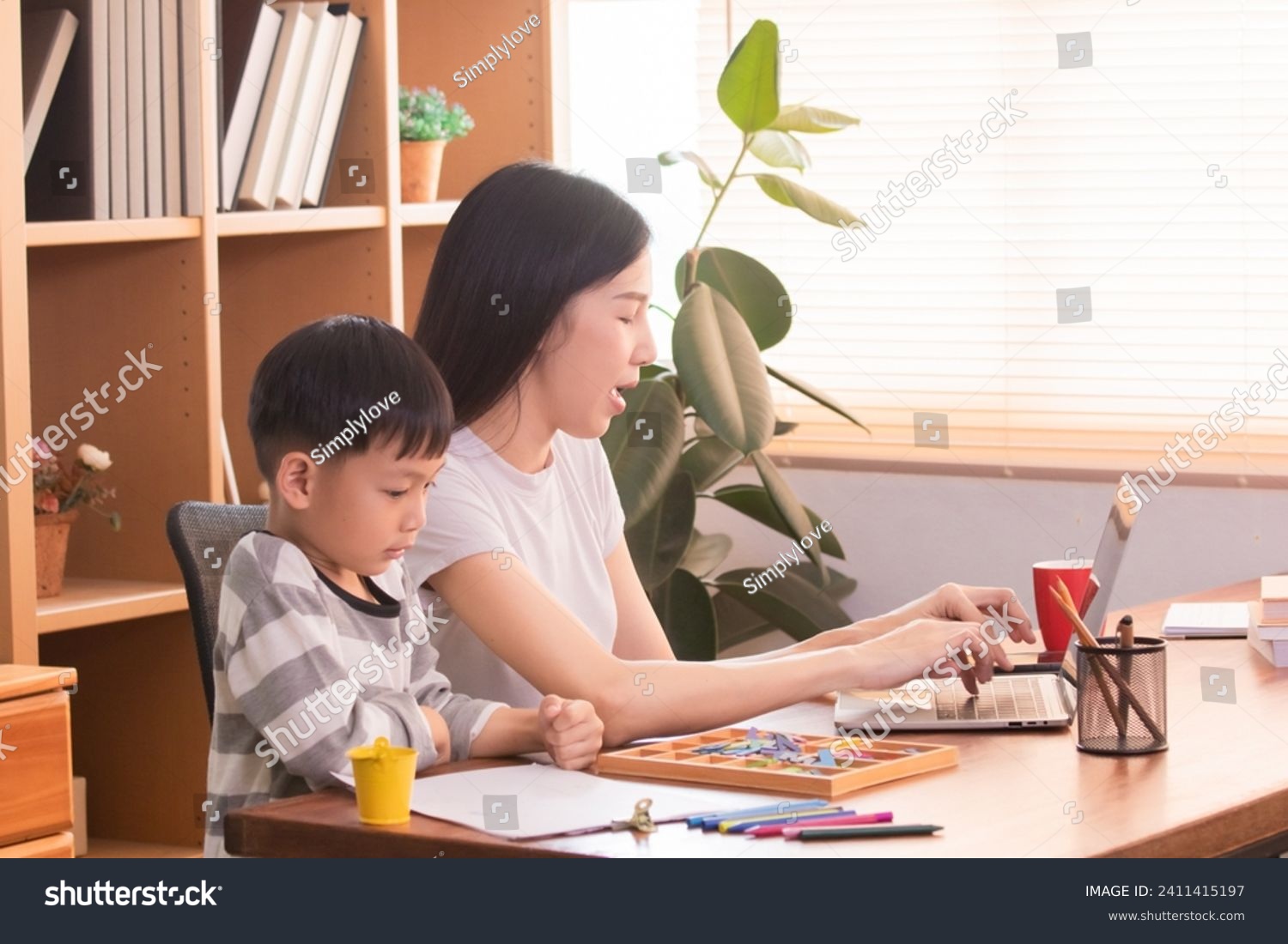Happy Asian single mother multitask spent time playing alphabet toys and drawing with little boy while working freelance or creative design remote work from home, young teacher teaching preschool kid #2411415197
