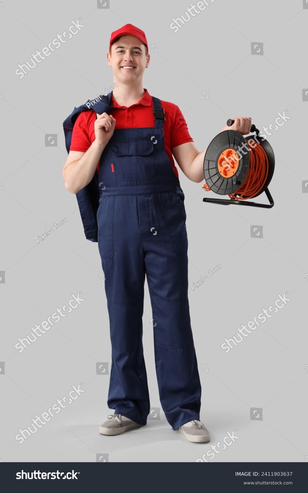 Male electrician with extension cord reel on light background #2411903637