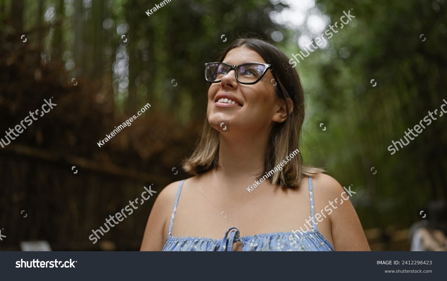 Beautiful hispanic woman with glasses, smiling confidently as she stands amongst kyoto's lush bamboo forest, looking around, full of joy and amazement. #2412296423