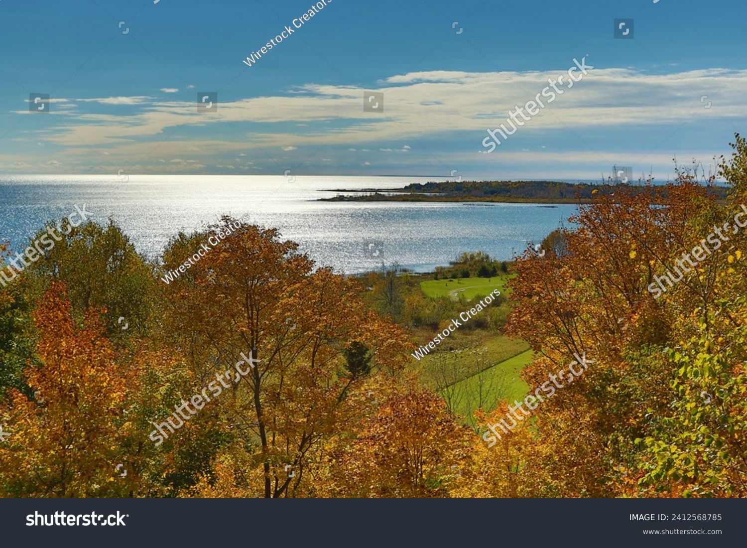 A picturesque scenery of a calm sea and blue sky captured from a shore with autums trees #2412568785