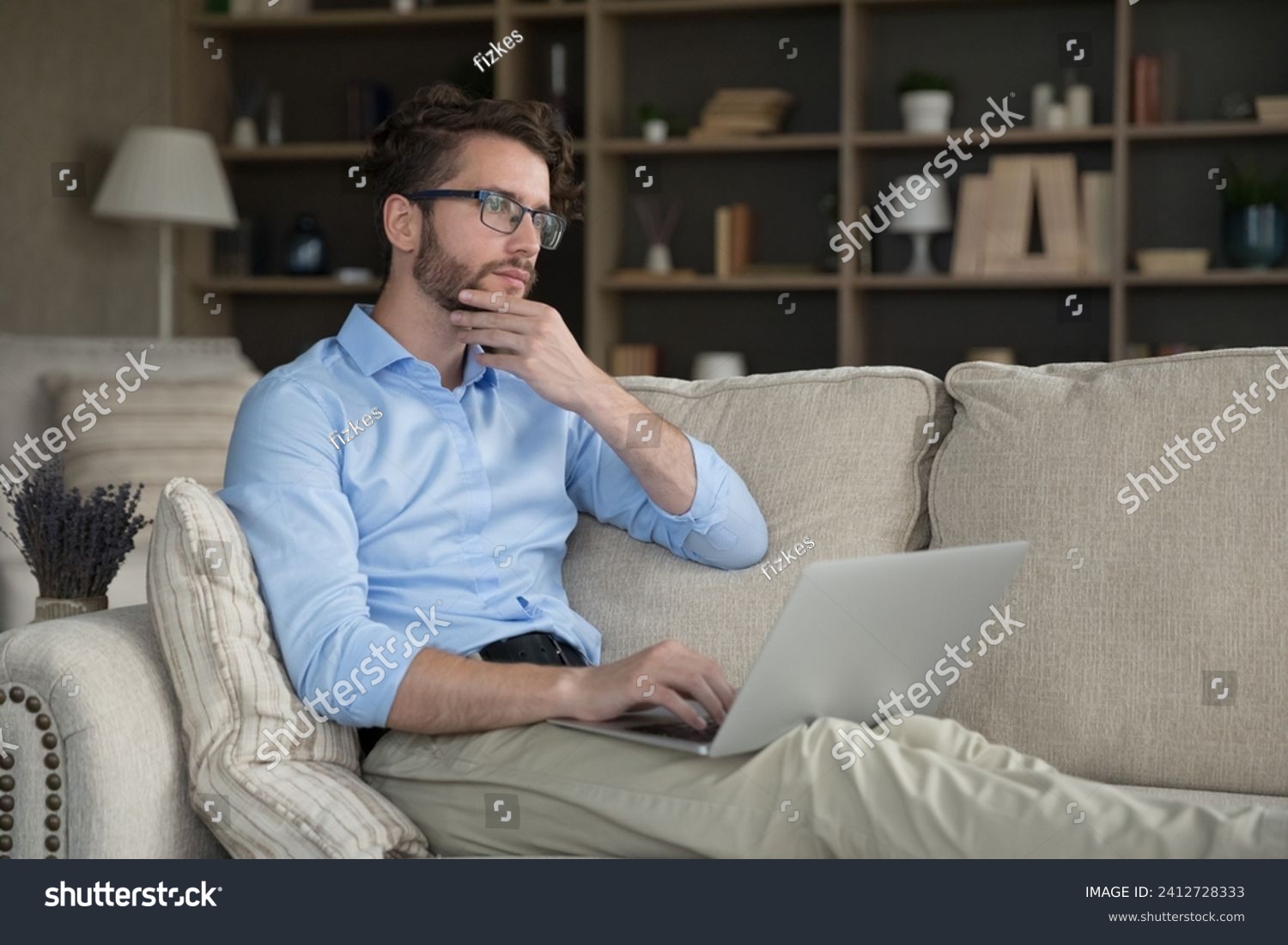 Serious thoughtful 35s man sit on sofa with wireless computer, get message, thinks on answer or creative online task, learn new AI program, looks pensive. Blogging, telework using laptop, modern tech #2412728333