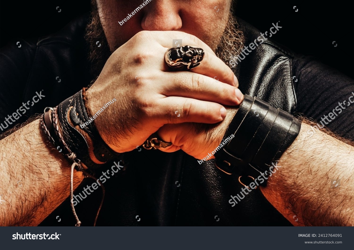 Close up photo of a shaded bearded male muscular biker with leather wrists, leather clothing, sitting by a table pose. #2412764091