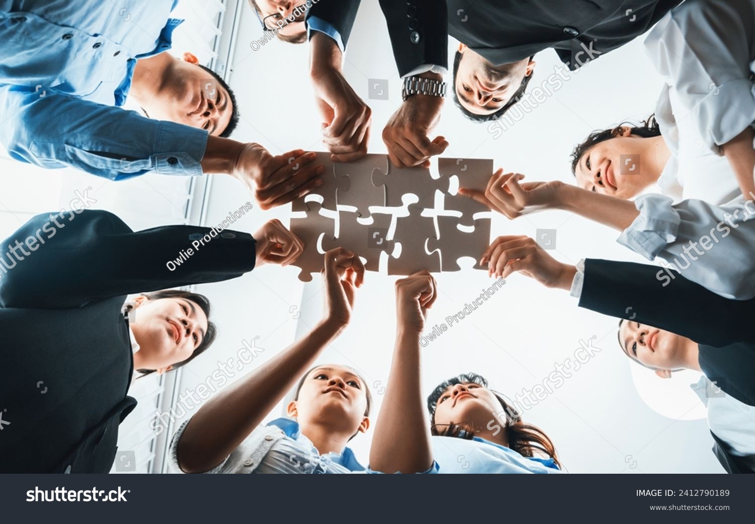 Multiethnic business people holding jigsaw pieces and merge them together as effective solution solving teamwork, shared vision and common goal combining diverse talent. Below view. Habiliment #2412790189
