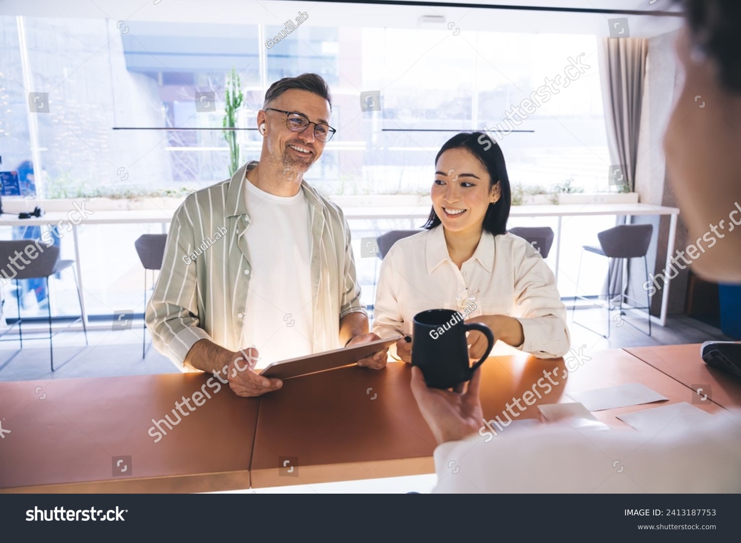 Happy male and female colleagues communicate with receptionist in corporate company, cheerful employees with touch pad technology talking with administrator about organization of business events #2413187753