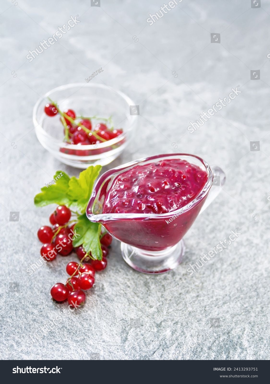 Red currant sauce in a glass sauceboat, berries in a bowl and on the table against the background of a granite table #2413293751