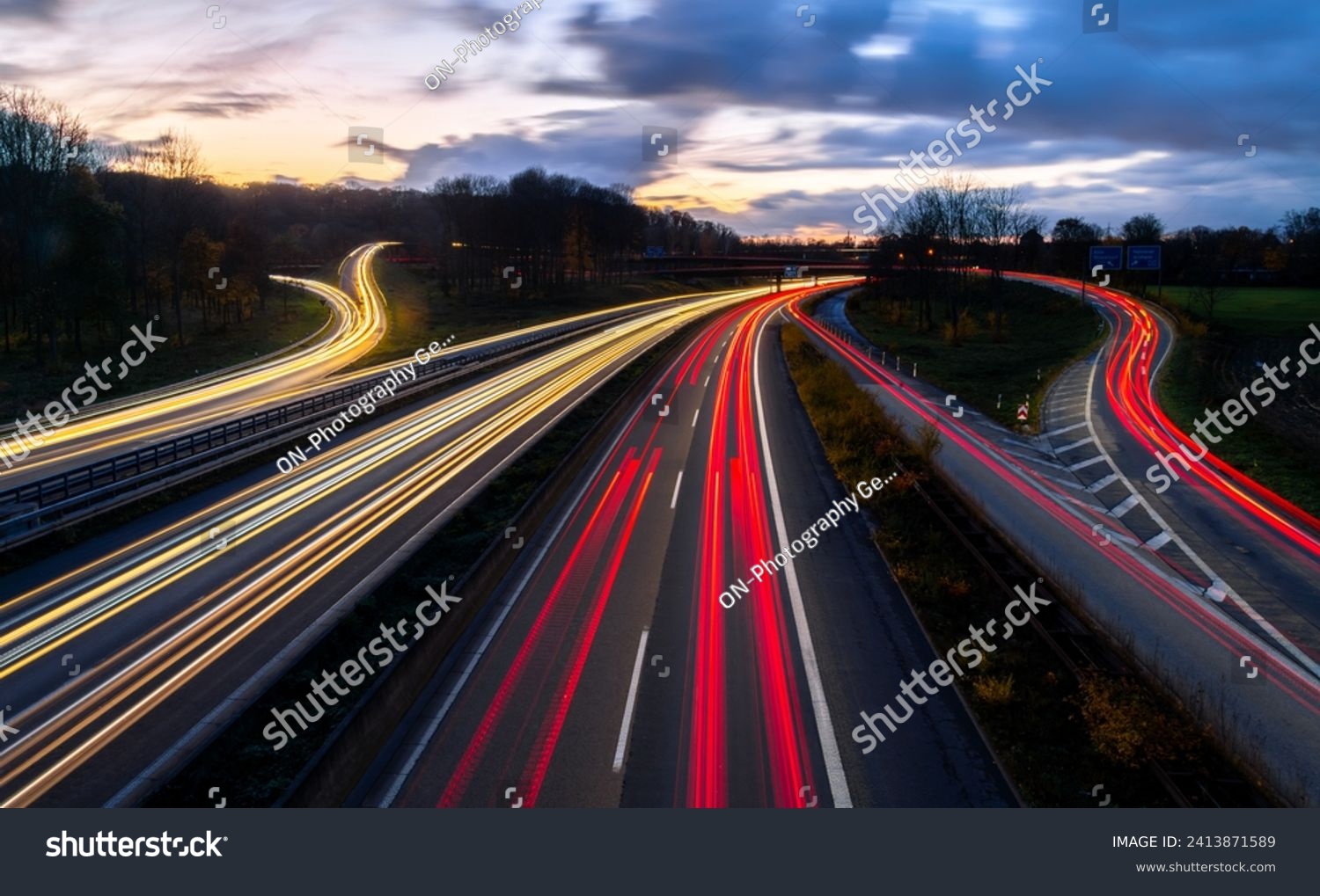 Autobahn crossing (A40 and A3) in Ruhr Basin Germany near Duisburg, Essen and Düsseldorf. Panoramic longtime exposure with red and white lights of passing cars at blue hour twilight after sunset. #2413871589