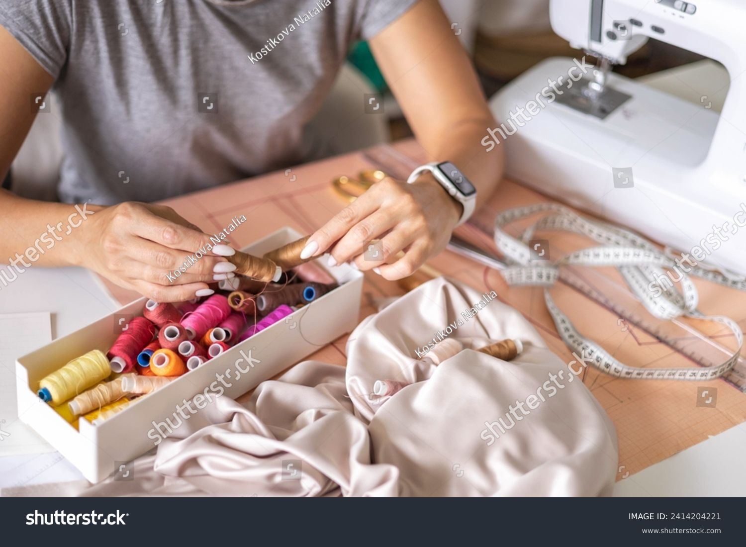 Woman dressmaker hands choosing thread color for sewing beige fabric clothes at workshop studio closeup. Female tailor fashion designer art work modist dressmaking professional occupation top view #2414204221
