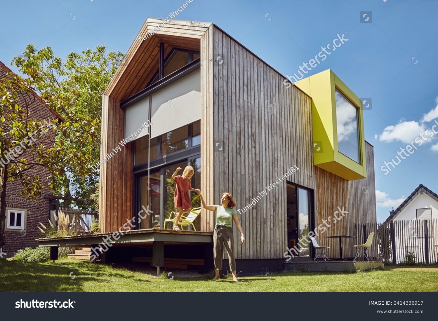Mother assisting daughter in jumping outside tiny house at yard #2414336917
