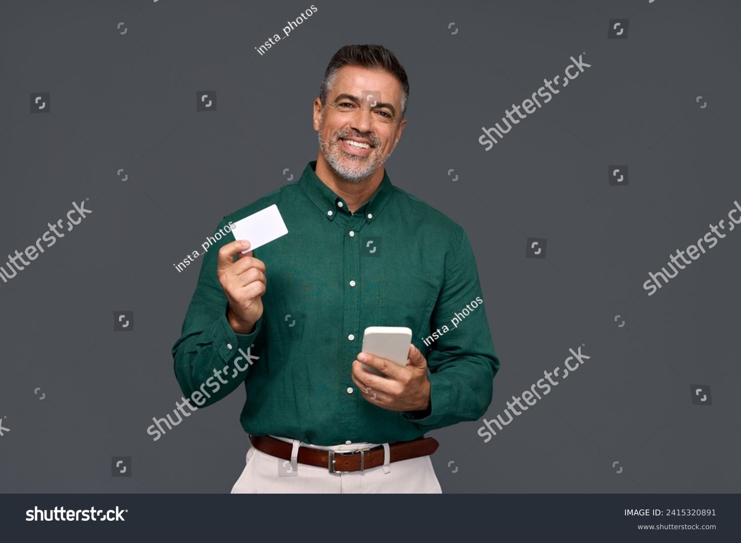 Happy middle aged business man, smiling mature businessman holding mobile phone and credit debit card mockup using banking finance app making online purchase on smartphone isolated on gray background. #2415320891