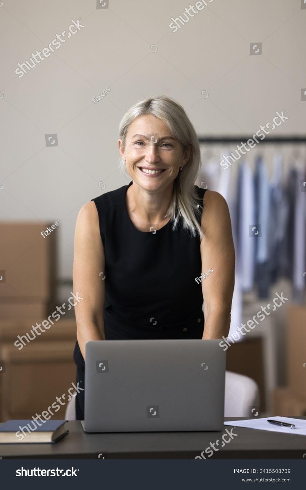 Portrait of middle-aged small business owner posing in warehouse. Female designer standing at desk with laptop at personal atelier workplace. Entrepreneurship, distribution, dropshipping, workflow #2415508739