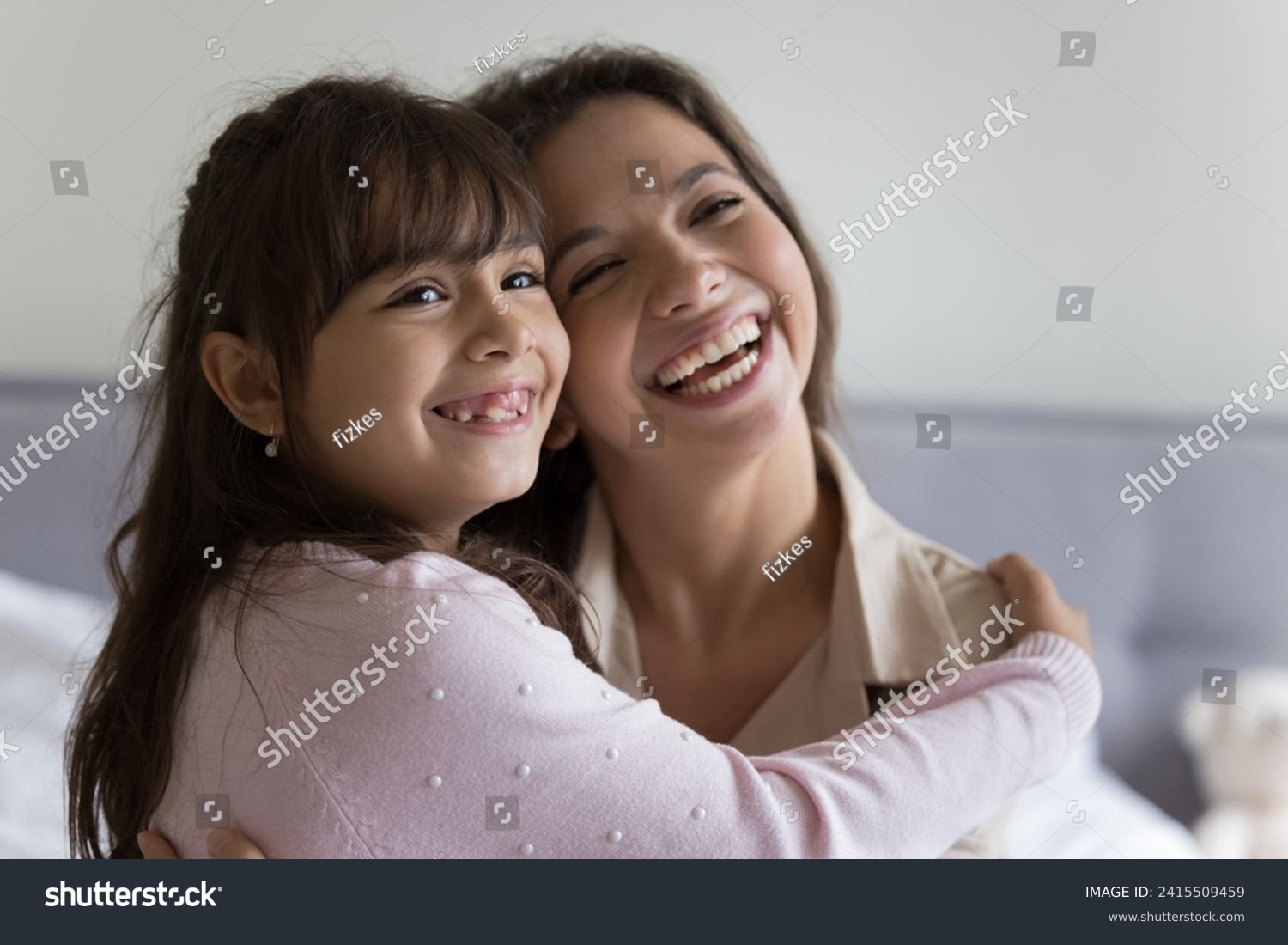 Close up of joyful little girl spend leisure time at home with loving mother, cute daughter hug caring young mom, smiling, look away, happy family express love and affection, enjoy strong family ties #2415509459