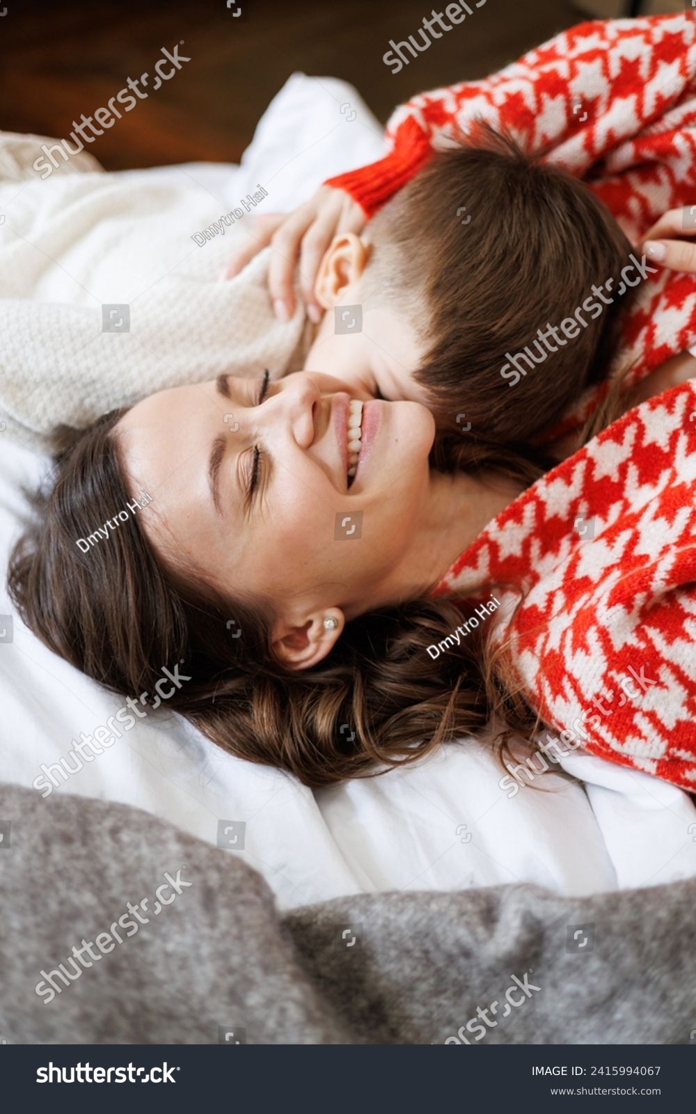 Toddler boy in sweater kissing happy mother on bed #2415994067