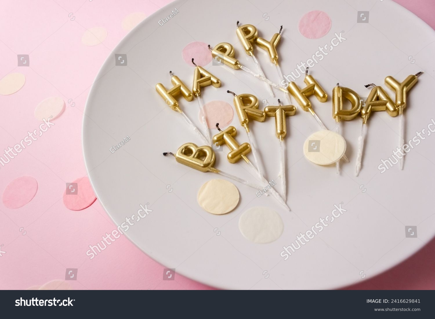 Used Happy Birthday candle letters on a party plate surrounded by confetti. Selective focus #2416629841