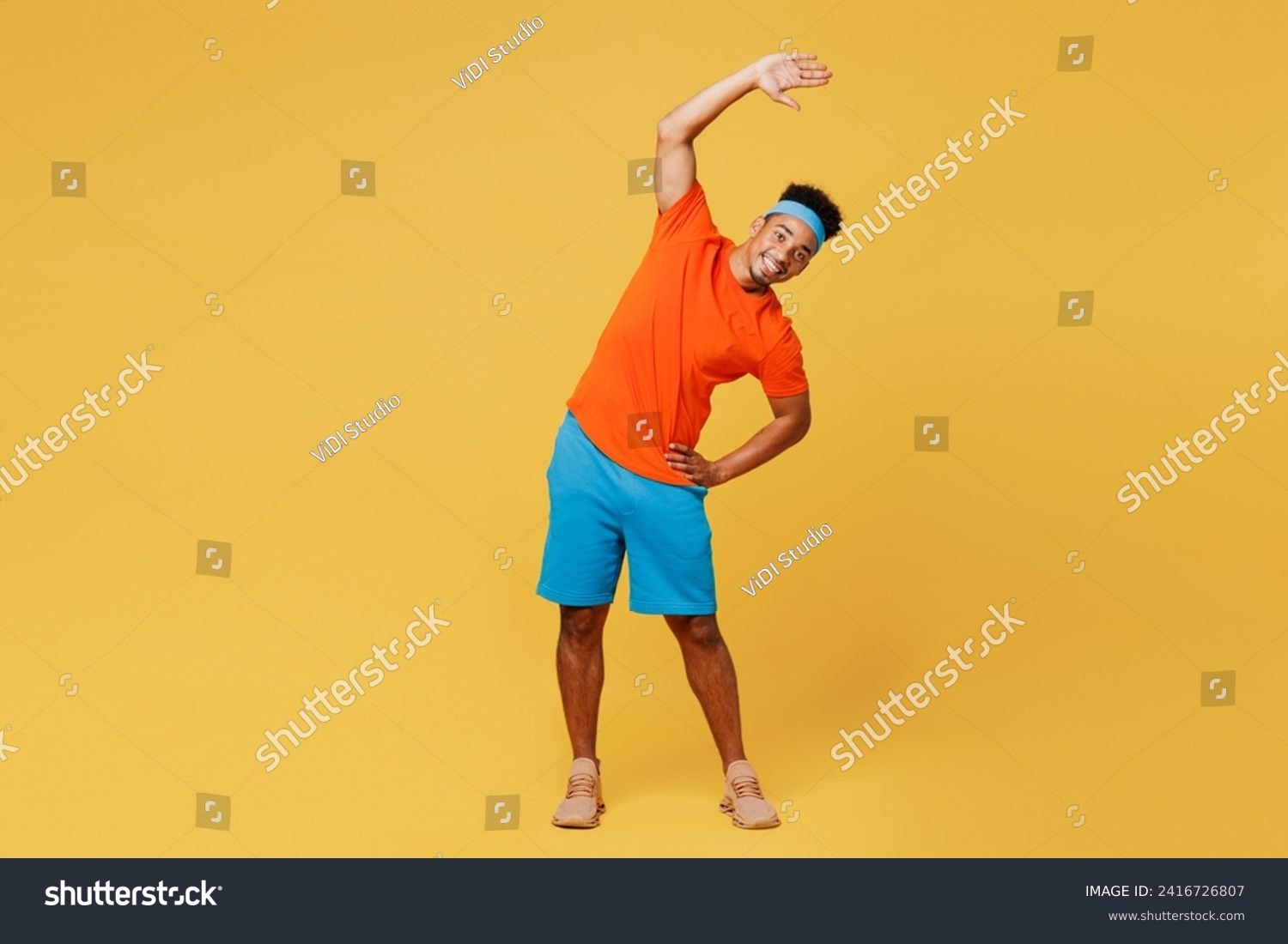 Full body young fitness trainer sporty man sportsman wear orange t-shirt do stretch lunge exercise rising hands up train in home gym isolated on plain yellow background. Workout sport fit abs concept #2416726807