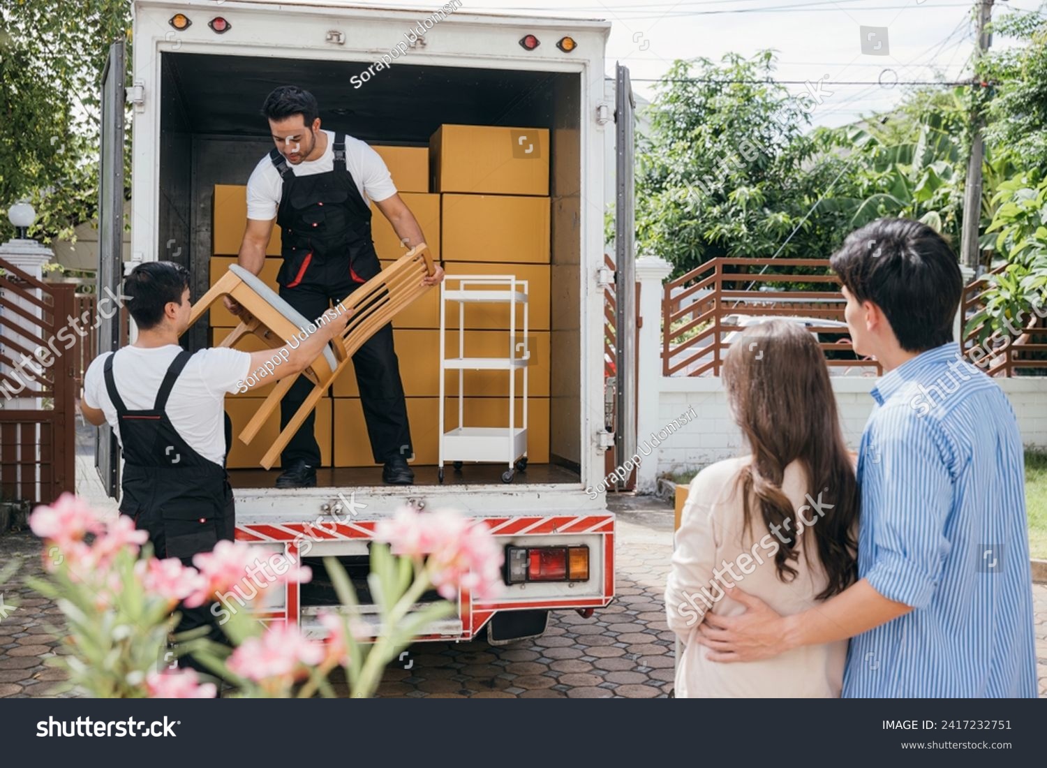Moving house made easy for a couple with the help of a professional delivery team. They work together unloading and lifting cardboard boxes for efficient relocation. Moving Day Concept #2417232751