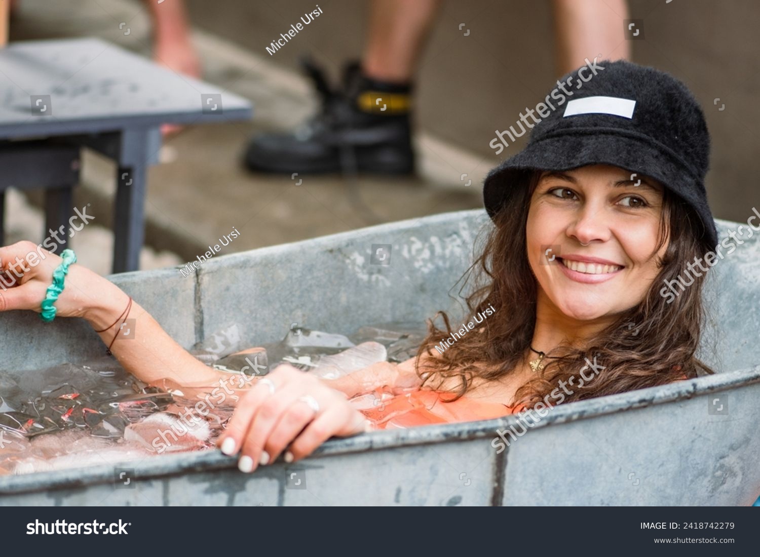 Pretty girl or woman wearing a hat, smiling and ice bathing in the cold water among ice cubes in a vintage bathtub. Wim Hof Method, cold therapy, breathing techniques, yoga and meditation #2418742279
