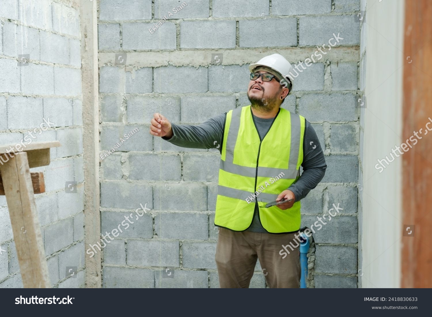 Asian male construction engineer, wearing full clothing, safety helmet, reflective vest, holding laptop in hand, checking work site for completeness, following construction plans. #2418830633