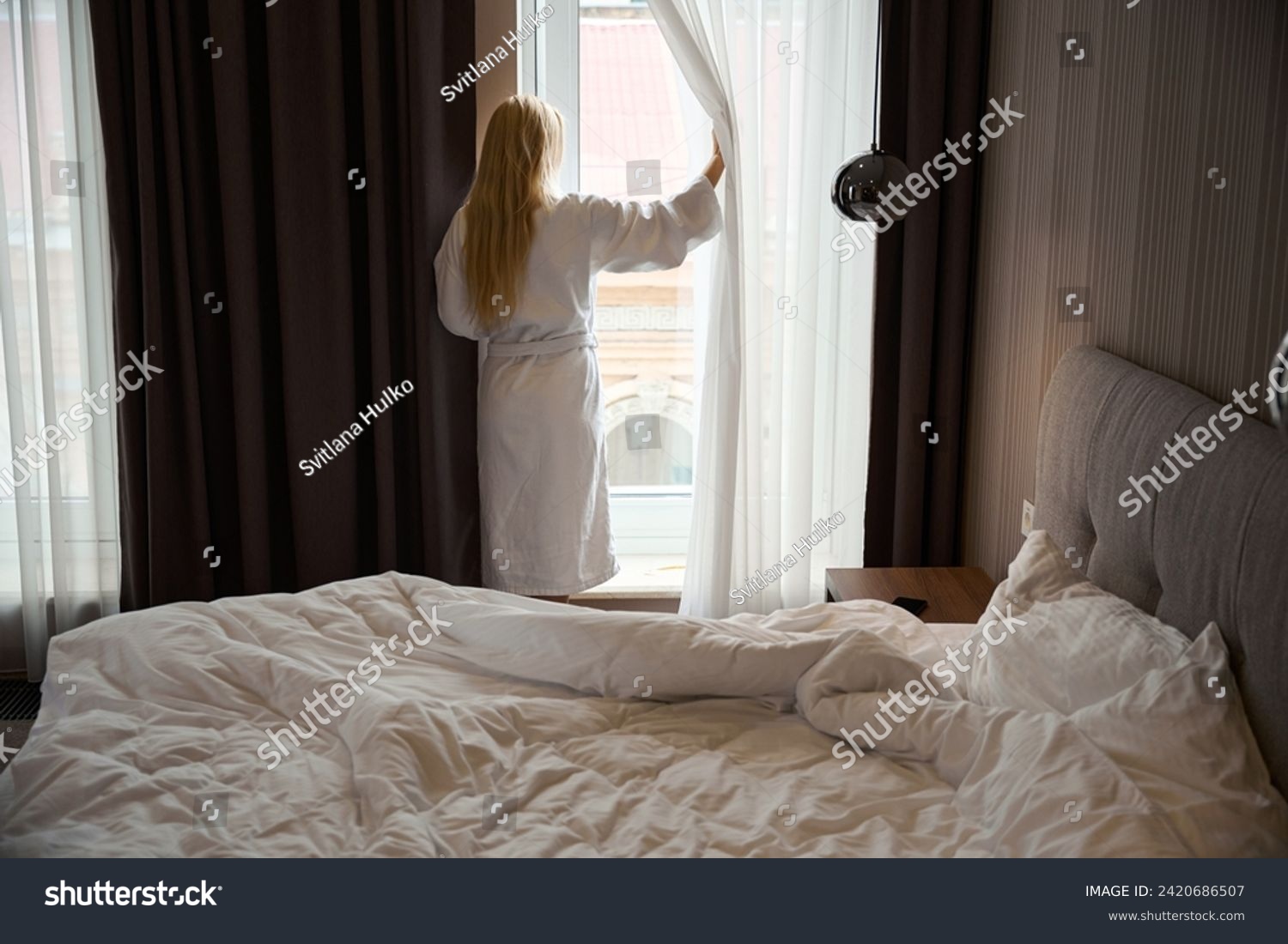 Woman standing in front of window in bedchamber after morning awakening #2420686507