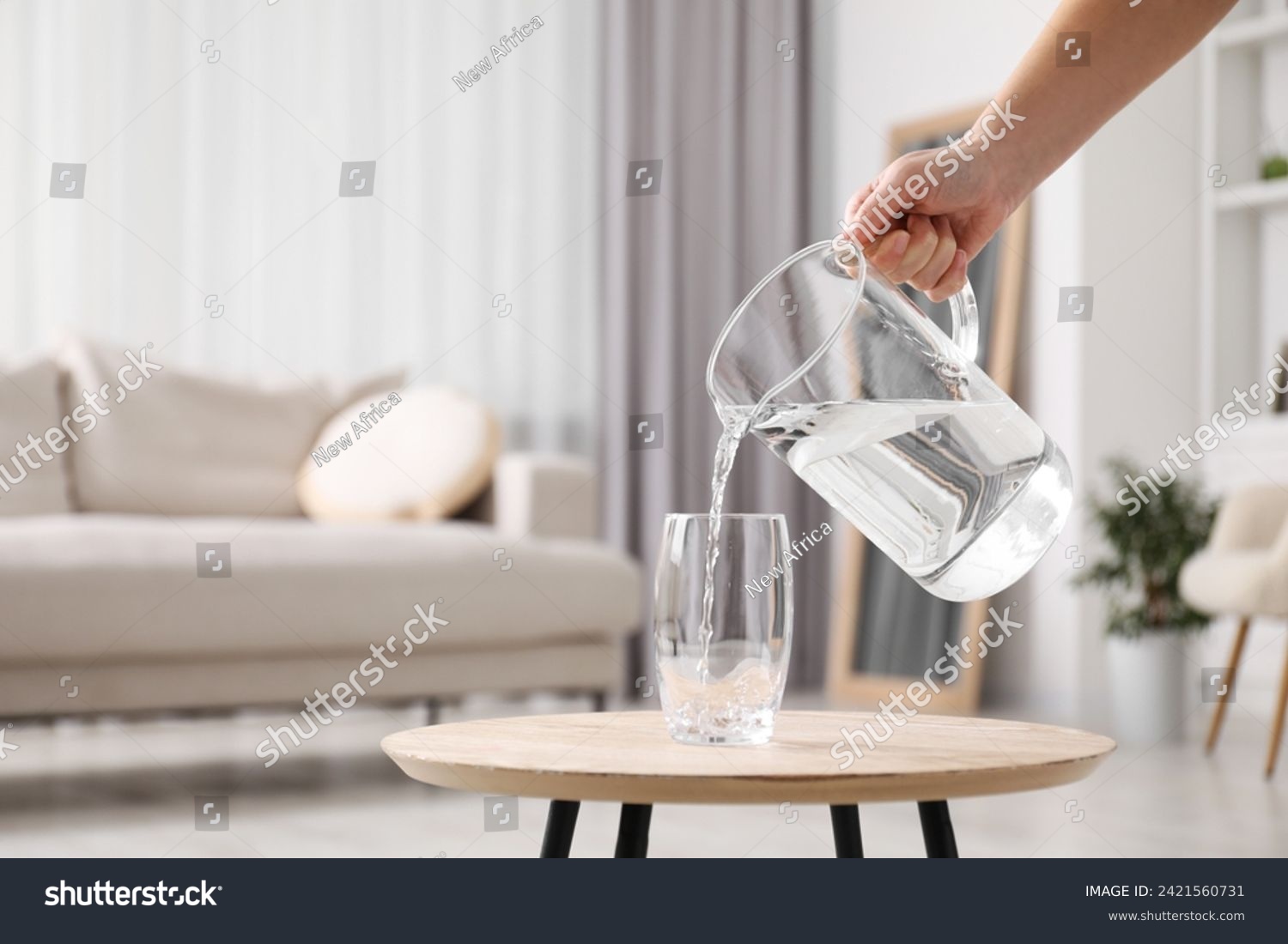 Woman pouring fresh water from jug into glass at wooden table indoors, closeup. Space for text #2421560731