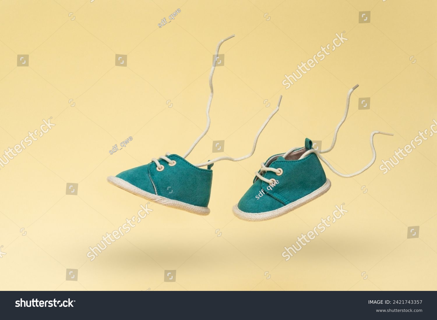 Flying baby shoes with flying laces on yellow background. Newborn baby concept with levitation effect and copy space #2421743357