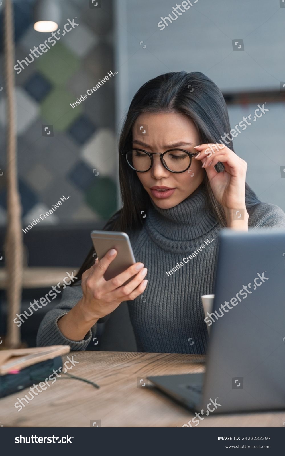 Vertical shot of working process. Young business woman with full concentration checking her mobile phone sitting on a table at coworking. Remote job, loan, mortgage, financial issues #2422232397