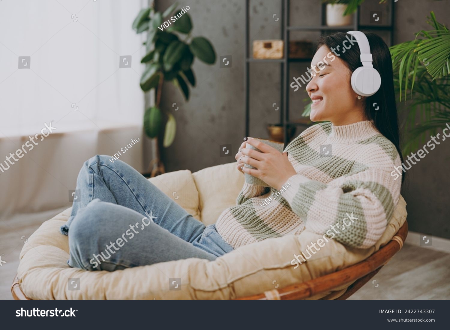 Full body young woman wears casual clothes listen to music in headphones drink tea sits on armchair stay at home hotel flat rest relax spend free spare time in grey living room indoor. Lounge concept #2422743307