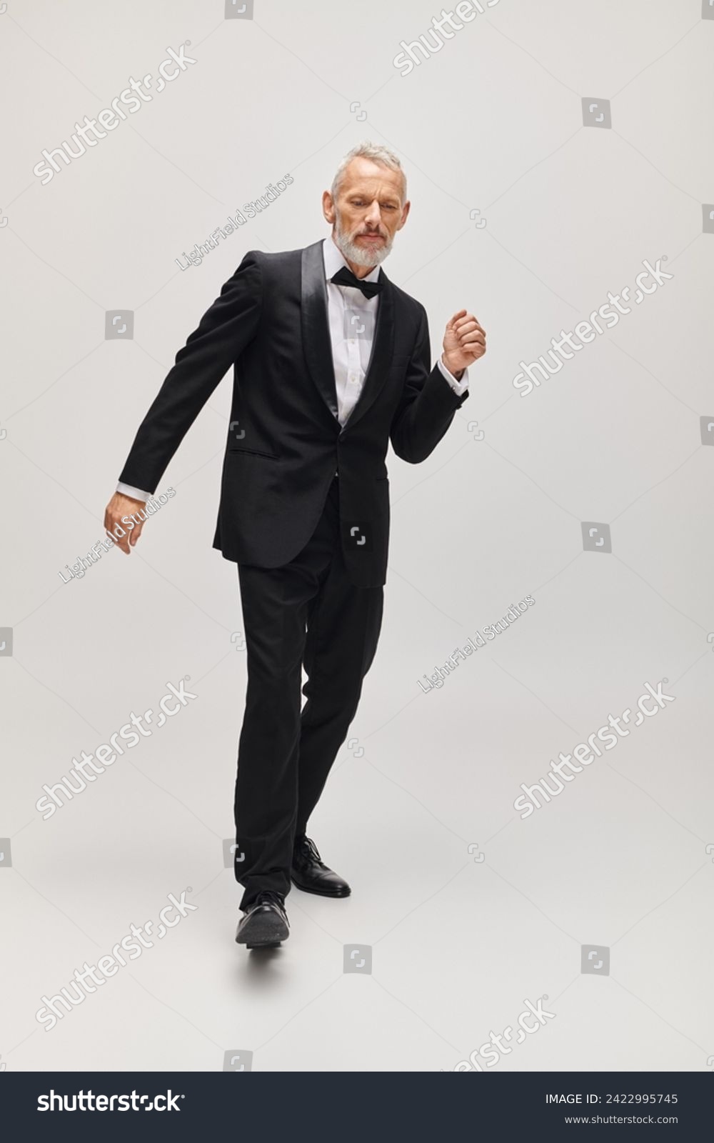 well dressed mature man with stylish bow tie in voguish tuxedo dancing actively on gray backdrop #2422995745