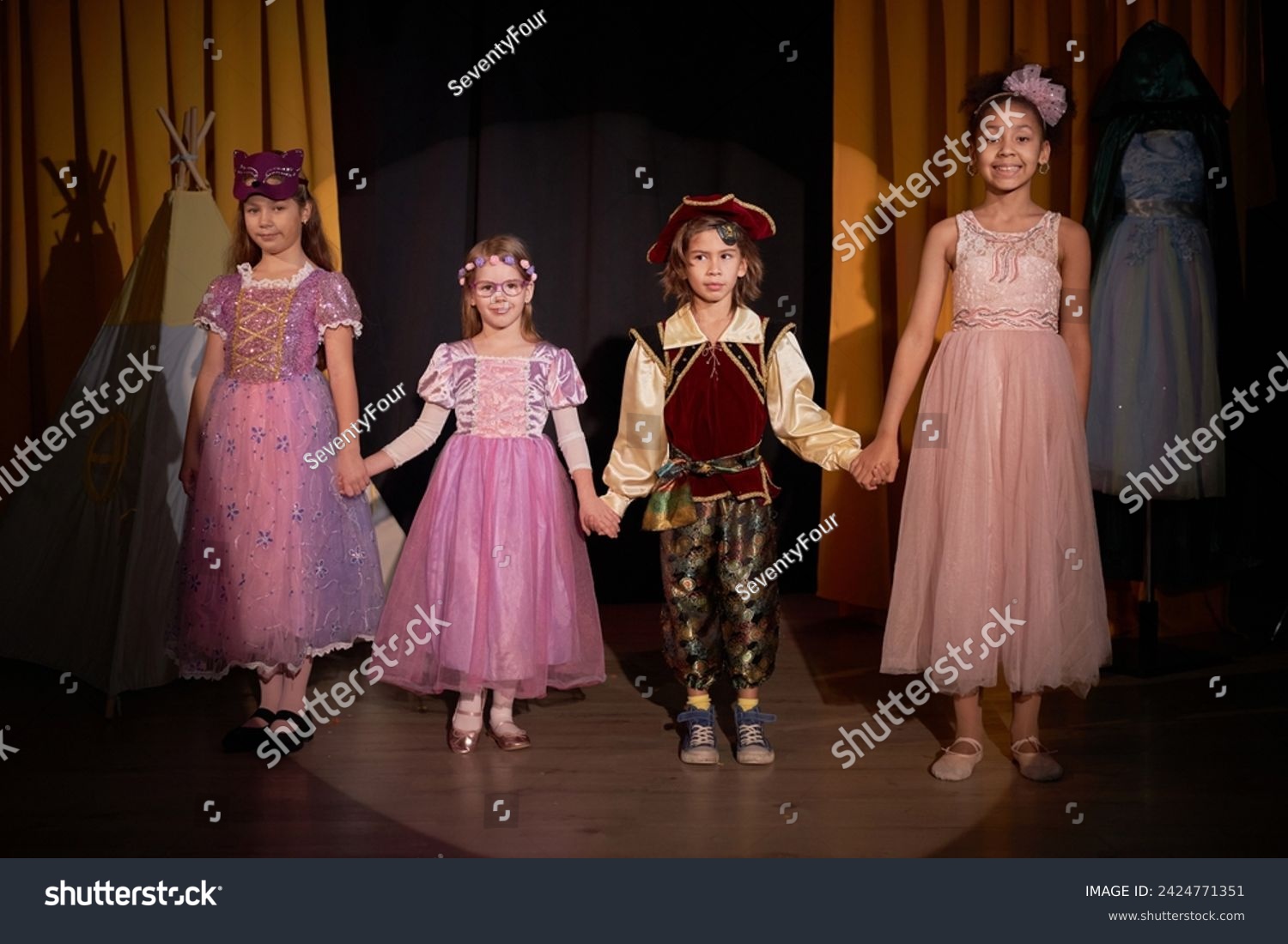 Full length portrait of group of children actors standing on stage holding hands for final bow at school play in theater #2424771351