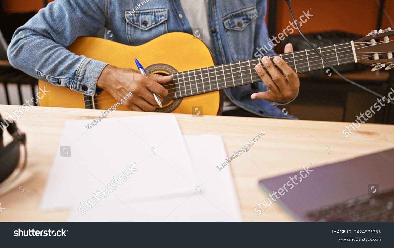 A young man composing music with a guitar in a studio setting, showcasing creativity and artistry. #2424975255