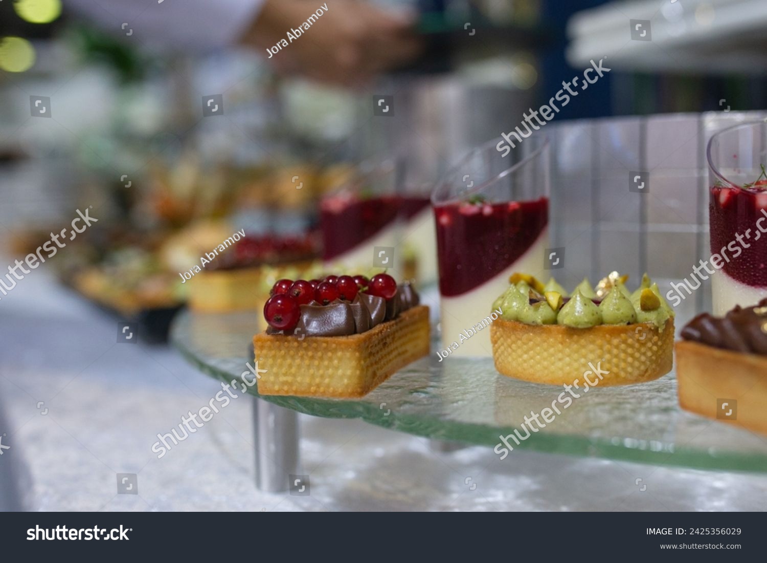 Variety of sweet and savory canapes and desserts displayed on glass shelf. Canapes topped with ingredients like caviar, salmon, and vegetables. Desserts include tarts, cakes, and pastries. #2425356029