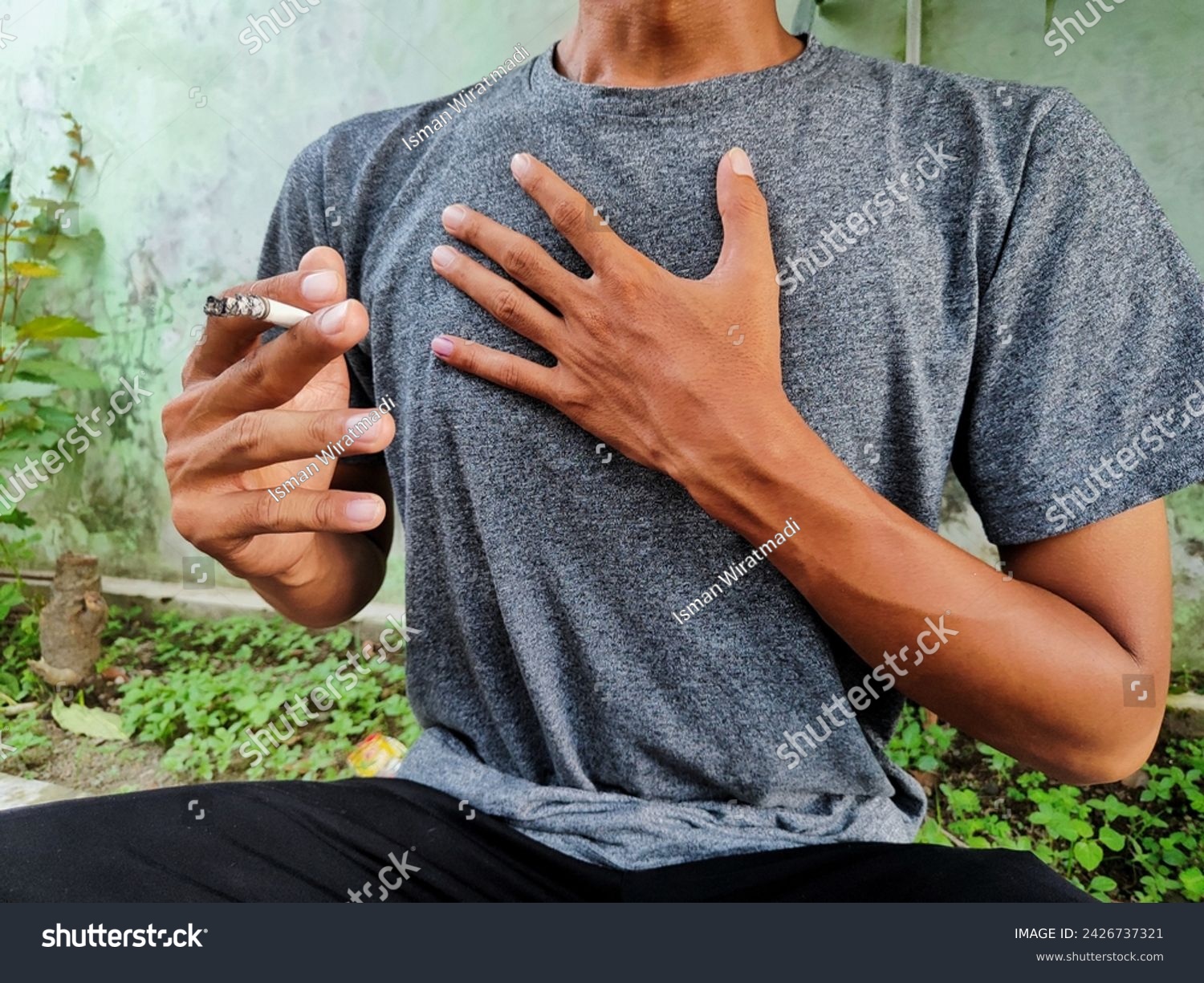 A man in gray clothes whose right hand is holding a cigarette and his left hand is holding a tight chest.  Men who experience respiratory problems due to smoking. #2426737321