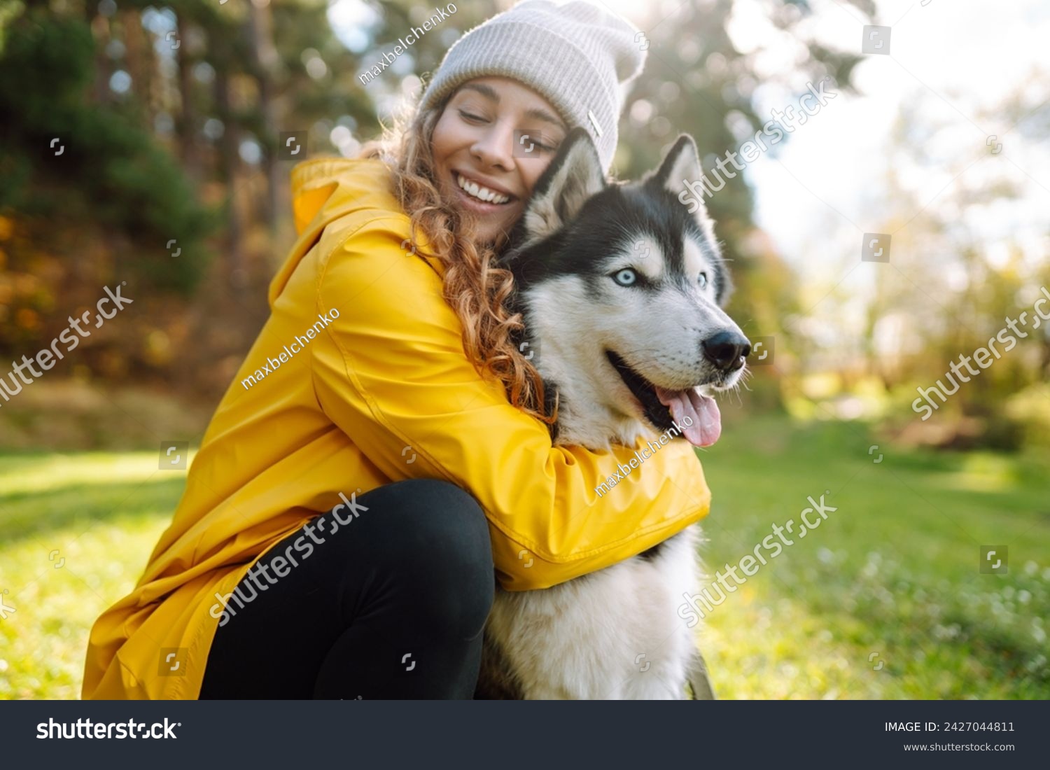 Beautiful young woman in a yellow coat walks in a park with her pet husky. A pet owner spends time with her dog. Concept of fun, entertainment. #2427044811