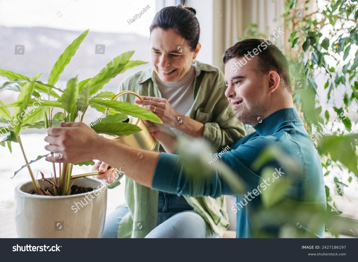 Portrait of young man with Down syndrome with his mother at home, taking care of plants. Concept of love and parenting disabled child. #2427186197
