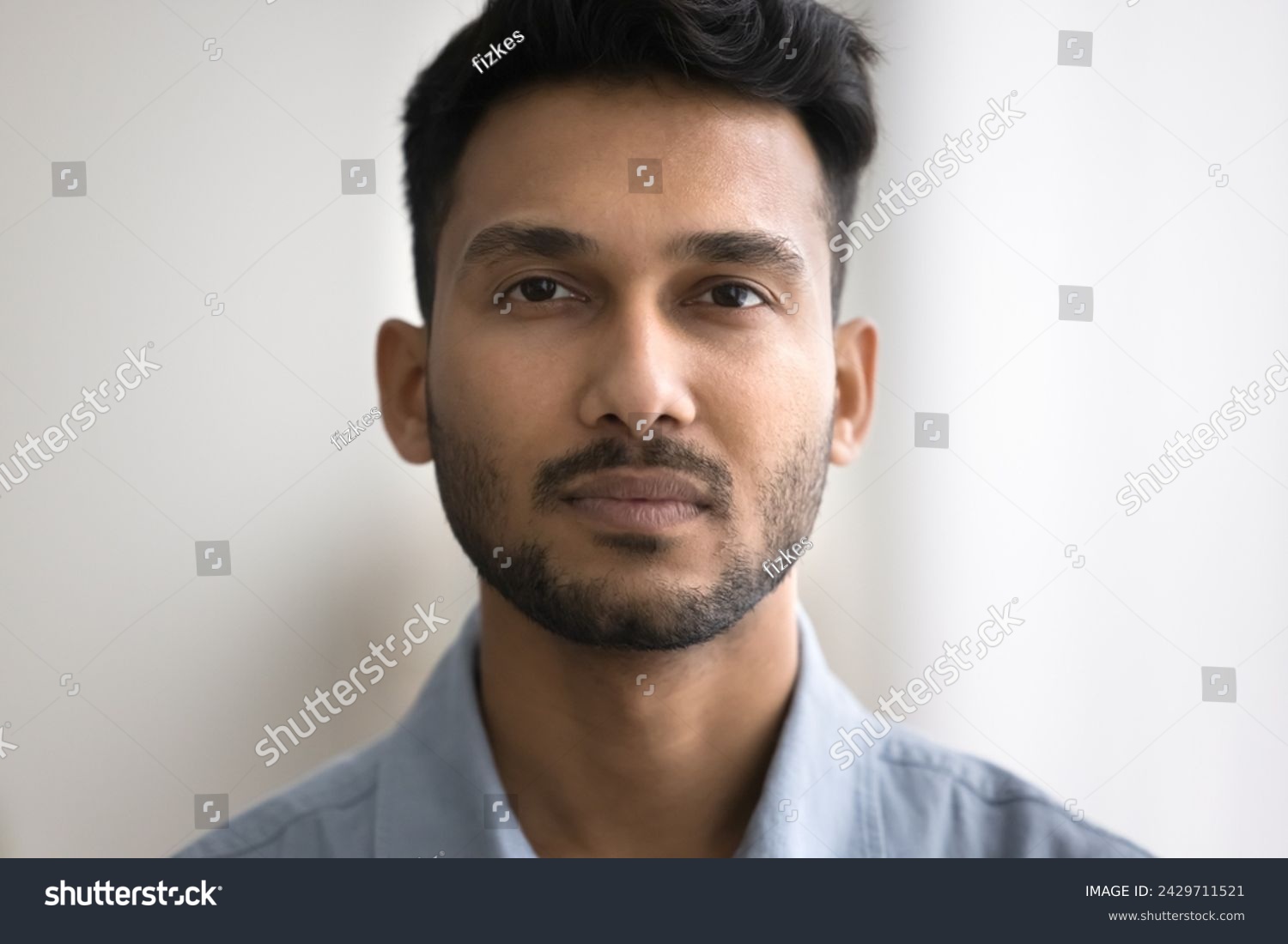 Close up of unsmiling Indian bearded guy standing indoor staring at camera. Man having attractive appearance, looks confident and serious. Millennial generation person, businessman head shot portrait #2429711521