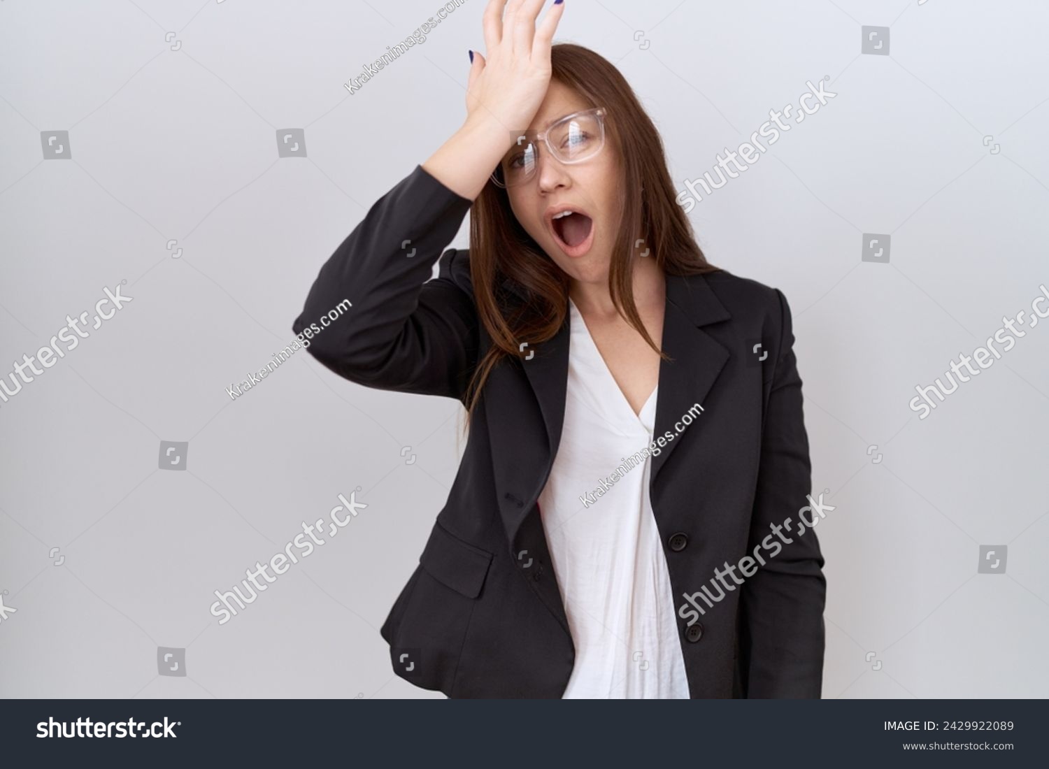 Beautiful brunette woman wearing business jacket and glasses surprised with hand on head for mistake, remember error. forgot, bad memory concept.  #2429922089