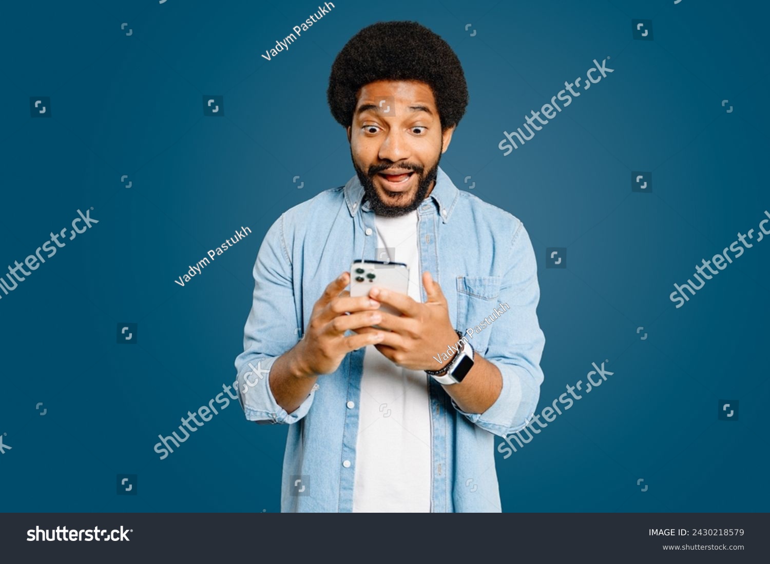 Young man looks surprised and excited using a smartphone, embodying a spontaneous moment of receiving unexpectedly good news, perfect for representing instant communication and its impact on emotions #2430218579