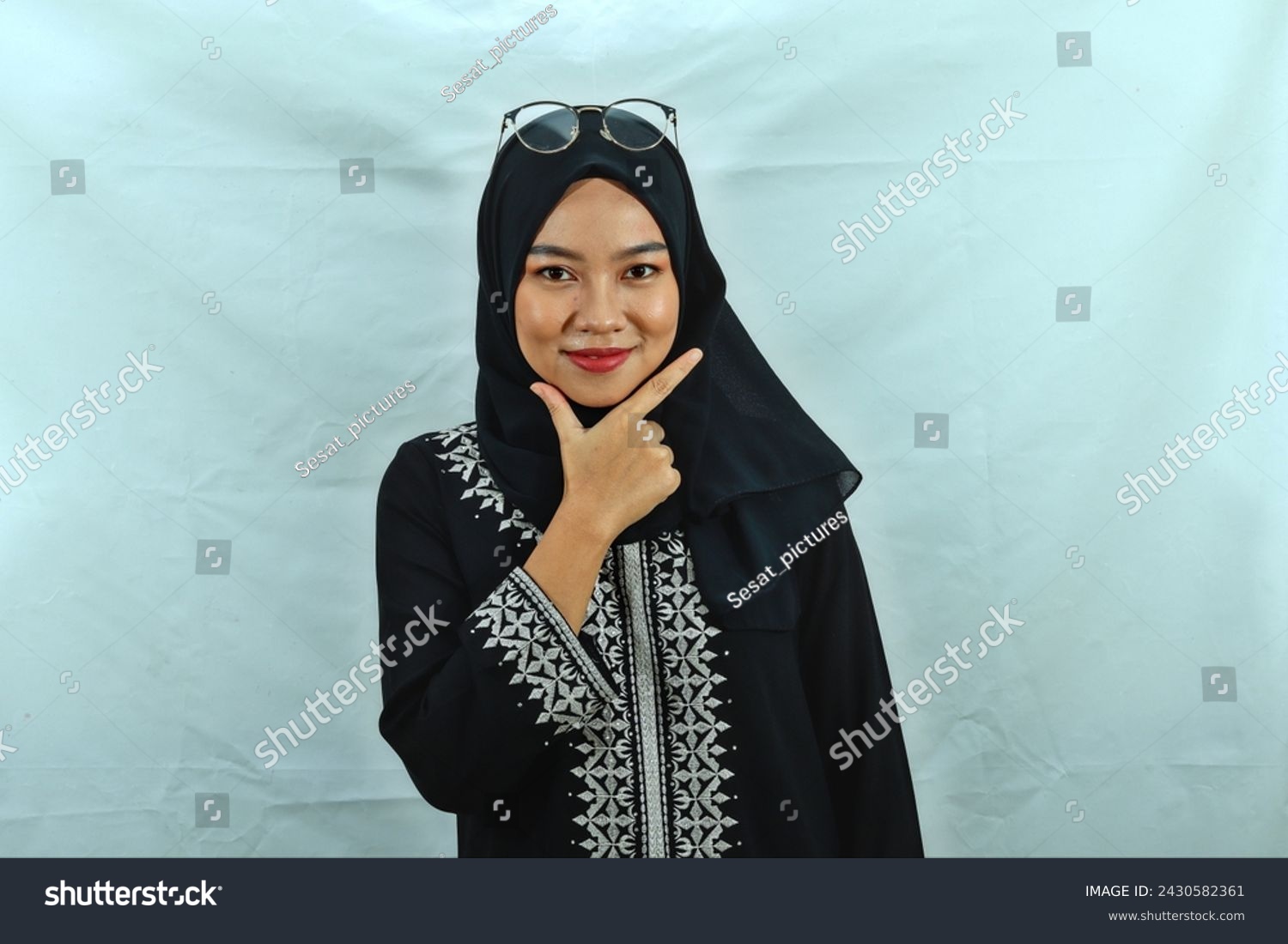 Asian Muslim woman wearing hijab, glasses and black dress with white pattern making chis gesture with a satisfied expression isolated on white background #2430582361