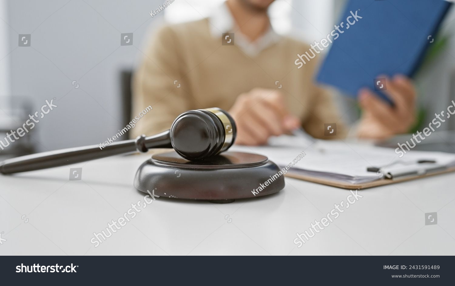 A focused man in a sweater reads a document in an office with gavel foreground emphasizing legal or judicial context. #2431591489