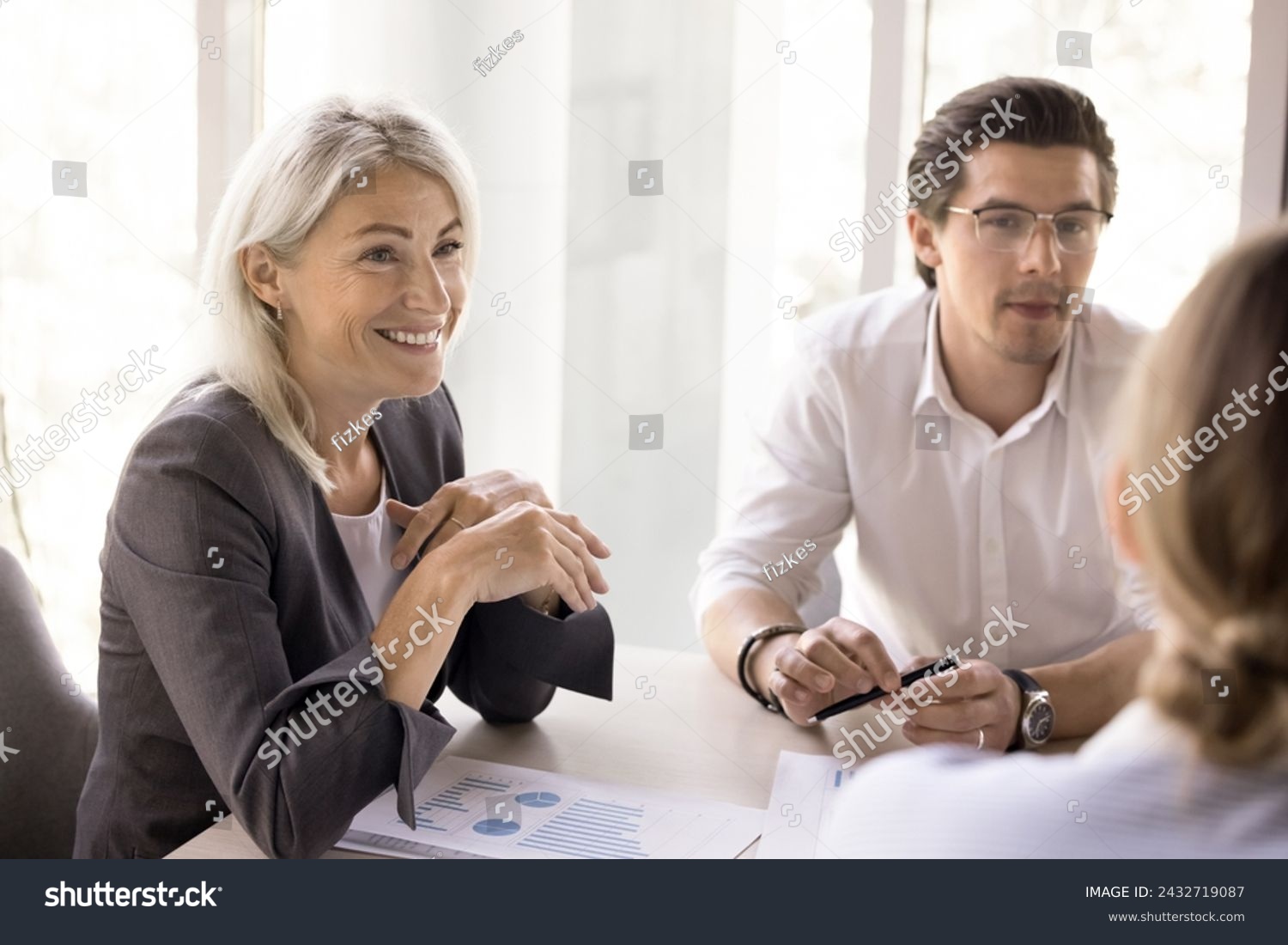 Mature smiling businesslady take part in meeting in office with colleagues, business partners, staff members to share ideas, express opinion, consider joint project, strategy discussion in boardroom #2432719087