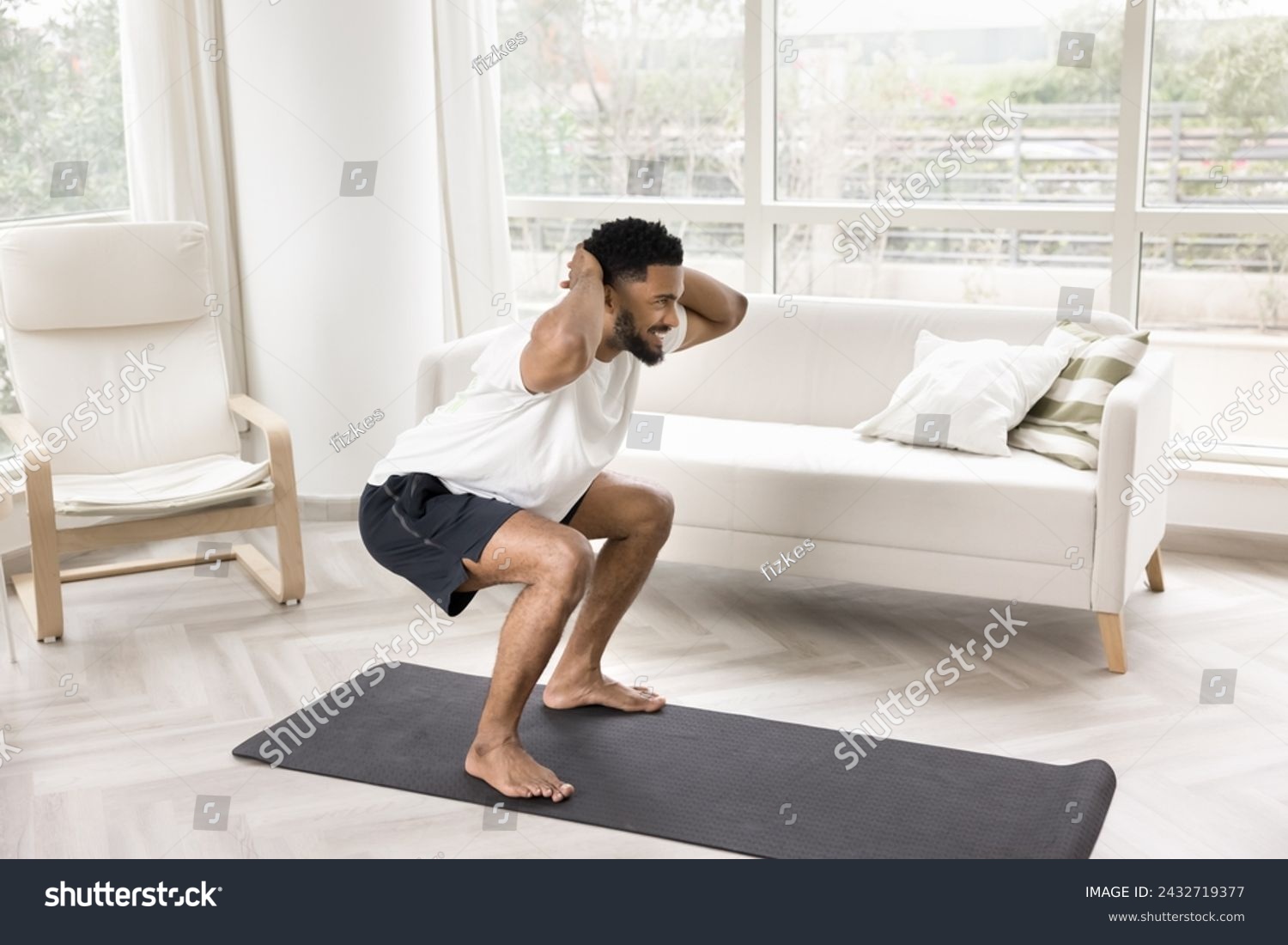 Happy sporty strong young African guy doing morning exercise on yoga mat at home, flexing hips, buttocks muscles in squats, looking away, smiling, enjoying active life style, keeping fit #2432719377
